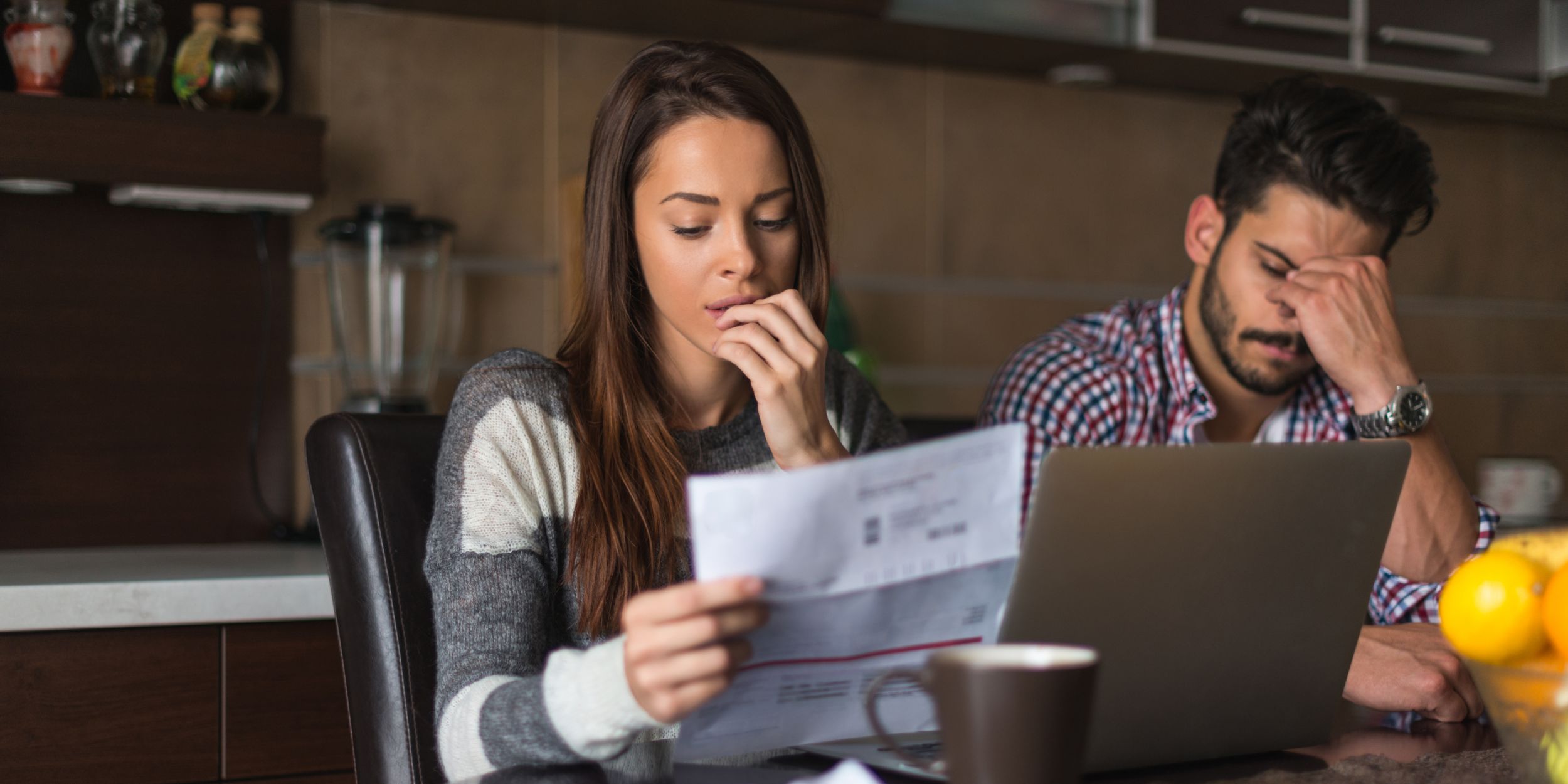 unpaid bills look on a womens face sitting at the table with her emotional support husband.